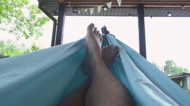 Relaxed view of bare feet resting in a blue hammock under a covered patio with string lights and bunting flags