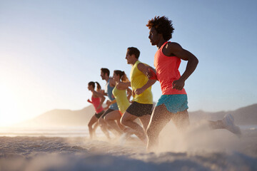 Dynamic shot of a diverse group running on a sandy beach towards a bright horizon. Represents teamwork, fitness, healthy lifestyle, determination, and achieving goals.