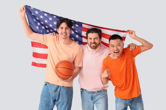 Male sports fans with ball and USA flag on light background