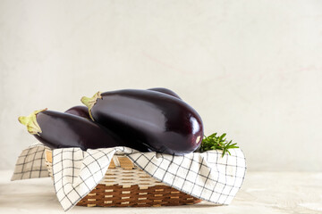 Basket with fresh eggplants and rosemary on light background
