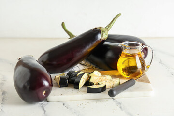 Fresh eggplants with pieces, knife and jug of oil on light background