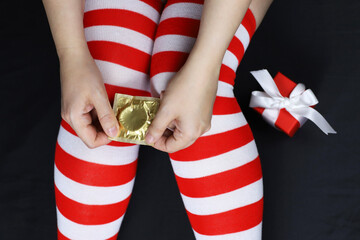 Woman with condom on the bed, contraception concept. Female legs in knee socks, romantic date in...