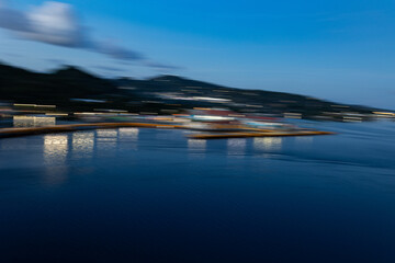 Abstract blurred night scene of a harbor and coastline with city lights reflecting on blue water.