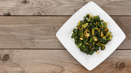 Cicoria Ripassata alla Romana, Roman-style chicory greens sautéed in olive oil with garlic and chili flakes. Rustic wooden background with space for text or logo.