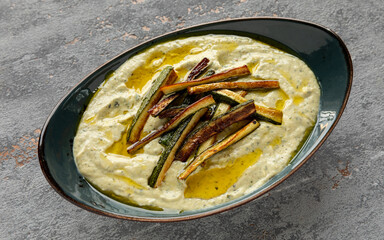 Courgette and tahini dip with fried zucchini strips and olive oil on top.