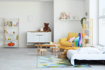 Interior of children's bedroom with bed, yellow armchair, bookshelf, commode, play table and toys