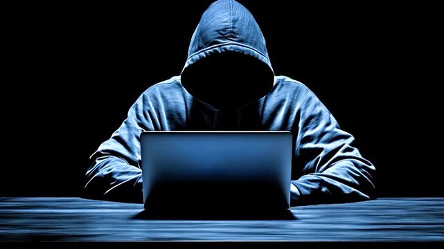 Image of a hooded hacker operating a laptop during a cyber attack