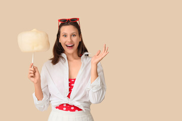Beautiful young happy woman with cotton candy on beige background