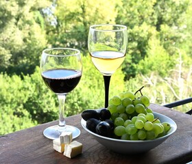 Outdoor wine tasting setup with red and white wine, fresh farm-to-table grapes, and soft cheese. Ideal for promoting vineyard tourism or gourmet product delivery.