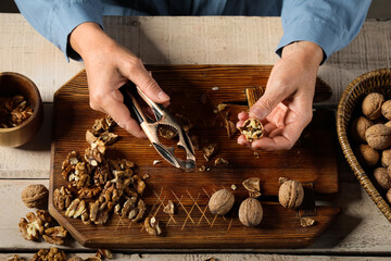 Elderly woman cracking walnuts with nutcracker on wooden table