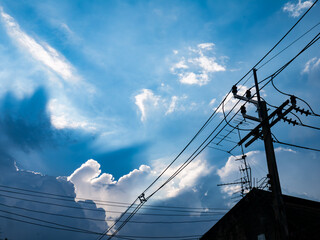 Dramatic blue sky with white cumulus clouds and electric power lines crossing diagonally in urban setting