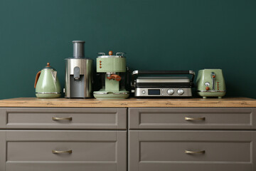 Different modern household appliances on counter against green wall