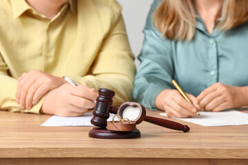 Couple with judge's gavel and rings on table signing divorce decree in lawyer's office, closeup