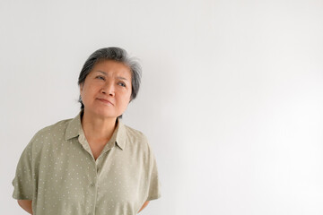Asian Thai elderly woman tilting head and smiling kindly, thoughtful isolated over white wall.