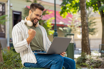 Overjoyed happy young man working on laptop netbook screaming in delight triumph winner gesture...