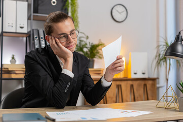 Serious Caucasian young businessman in formal suit sitting at home office with letter, upset and disappointed, reading bad news, receiving notification of bank loan refusal, frustrated by bankruptcy.