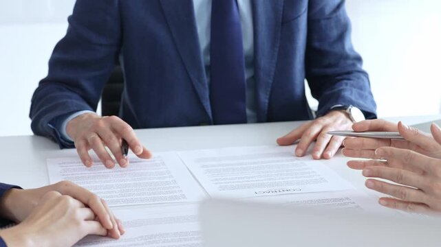 Business people meeting in an office, discussing important documents, pointing to a contract for signature, finalizing a deal, negotiating agreement terms, financial transaction concept