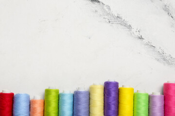 Row of colorful thread spools on marble background