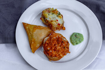 Delicious appetizer plate with samosa, bruschetta, and a vibrant green sauce