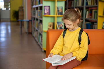 Portrait of a 7-8-year-old blonde girl in a yellow longsleeve in a library with books
