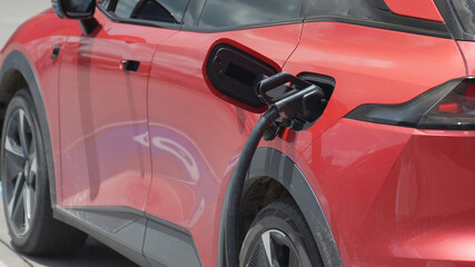 Bright red electric vehicle (EV) charging port open with a black charging cable plugged in, illustrating sustainable power, future transportation