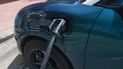 Dark teal blue electric vehicle (EV) being charged with a black nozzle and cable plugged into the charging port, highlighting clean energy, sustainable automotive technology