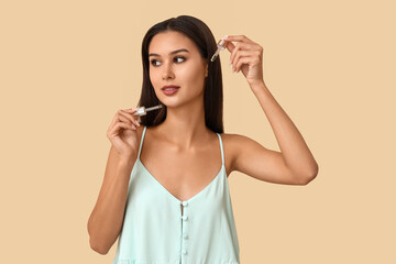 Fototapeta premium Beautiful woman holding serums with vitamin E on beige background