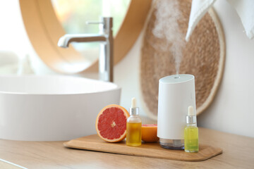 Modern air humidifier with essential oils and grapefruit on table in bathroom, closeup