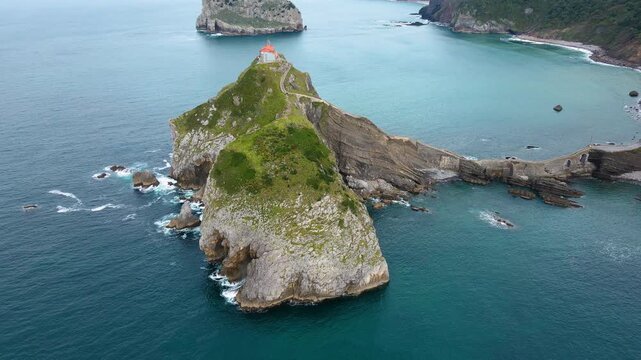 Aerial drone footage of San Juan de Gaztelugatxe, the iconic islet on the Basque coast of Spain. The video captures sweeping cinematic views of the winding stone bridge, the hermitage perched atop the