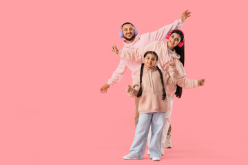 Happy parents with their little daughter in headphones dancing on pink background