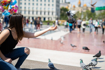 Joyful young woman feeding pigeons in a sunny city square, enjoying a peaceful moment surrounded by urban life and historical architecture on a vibrant afternoon adventure