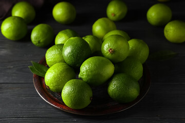 Plate with fresh ripe limes on black wooden background, closeup