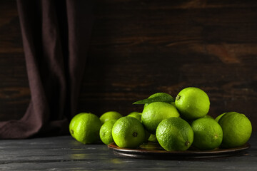 Plate with fresh ripe limes on black wooden table
