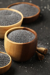 Wooden bowls with poppy seeds on black background, closeup