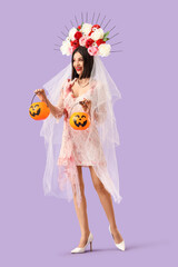 Beautiful young happy woman dressed as dead bride for Halloween with pumpkin baskets on purple background