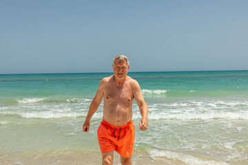 attractive senior man at the beautiful sandy beach in swim suit