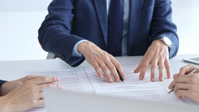Business people meeting in an office, discussing important documents, pointing to a contract for signature, finalizing a deal, negotiating agreement terms, financial transaction concept