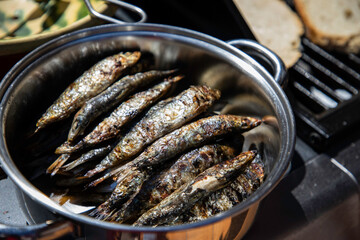 Grilled sardines in a silver bowl, ready to eat outdoors, offering a delicious taste of summer with a rustic vibe, perfect for food blogs, culinary events, and healthy eating campaigns