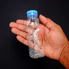 Damaged plastic bottle in hand black background closeup view 