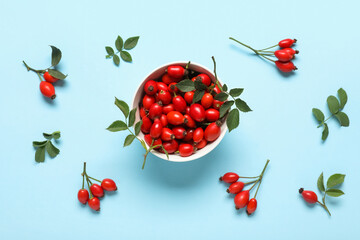 Bowl with fresh rose hip berries and leaves on blue background