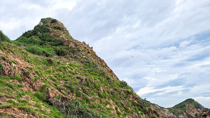 Dramatic Steep Mountain Peak Covered In Lush Green Vegetation Under A Cloudy Sky