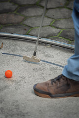 Miniature golf in action. A player putts an orange ball with a focus on their shoe and club, perfect for leisure activity articles.