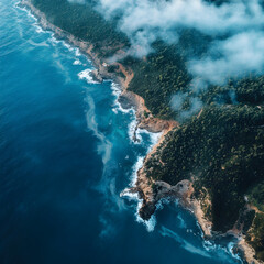 Obraz premium Aerial view of rugged coastline with turquoise ocean waves and lush green forest under misty clouds