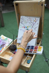 Hand-painting watercolor art on canvas outdoors with a tree sketch in focus.  Person painting on canvas, realistic style, with an outdoor neutral background