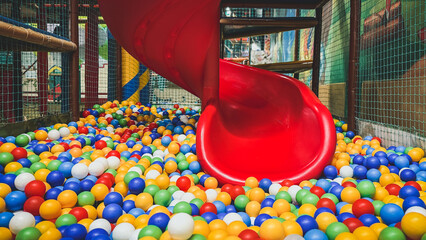 Bright red spiral slide ending in colorful ball pit inside indoor playground, filled with multicolored plastic balls, soft structures safety nets, perfect for children s fun entertainment activities