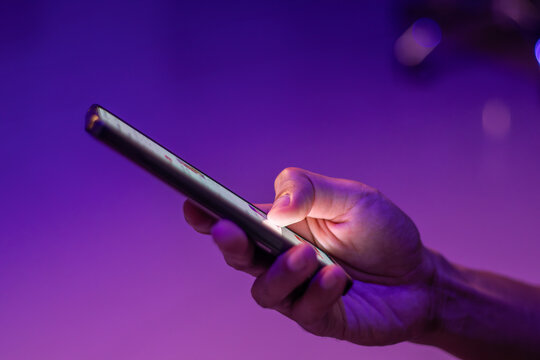 A man scrolling on social media apps or searching for information online on his smartphone on blue and purple neon lights background