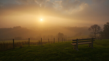 Misty sunrise over rolling hills with a wooden bench in the foreground