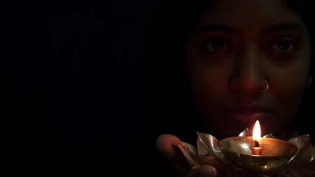 Beautiful Asian Indian girl holds a burning diya in her hands during the Diwali festival, celebrating Deepavali &mdash; the Hindu festival of lights &mdash; with a glowing traditional lamp in festive background.