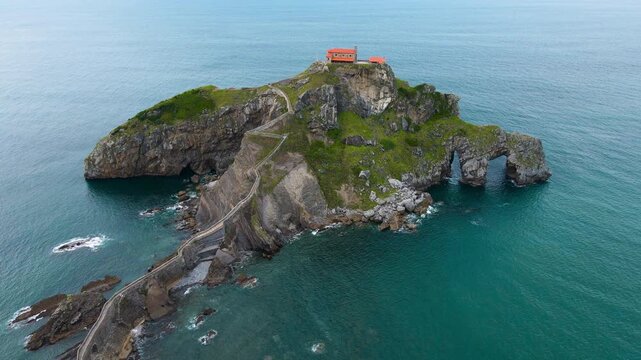 Aerial drone footage of San Juan de Gaztelugatxe, the iconic islet on the Basque coast of Spain. The video captures sweeping cinematic views of the winding stone bridge, the hermitage perched atop the