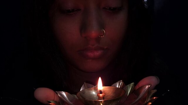 Beautiful Asian Indian girl holds a burning diya in her hands during the Diwali festival, celebrating Deepavali &mdash; the Hindu festival of lights &mdash; with a glowing traditional lamp in festive background.